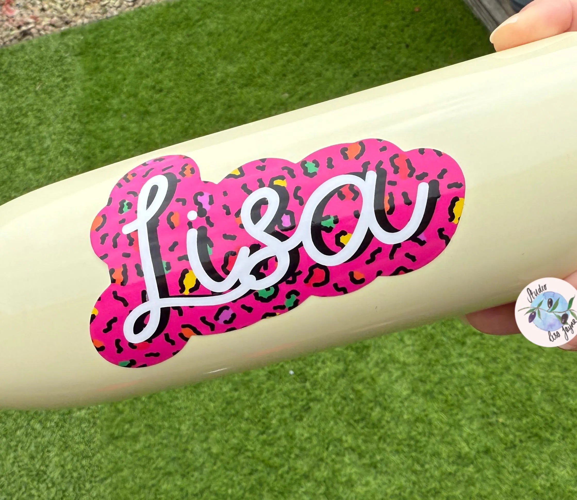 Beige water bottle with a pink and multicolor leopard print 'Lisa' sticker on a grass background
