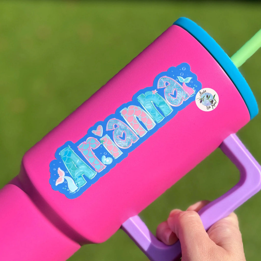 Pink and purple watr drink bottle with 'Arianna' Mermaid themed sticker on it against a green background