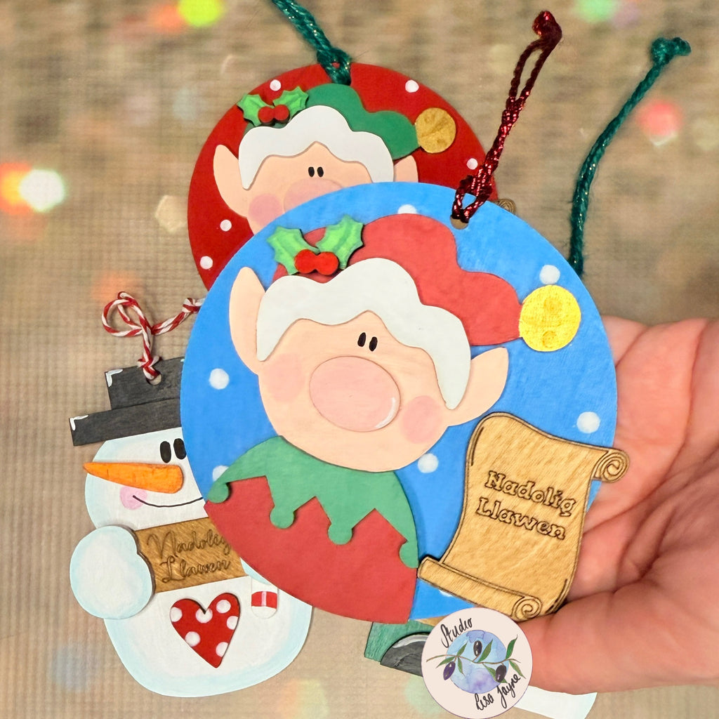 Nadolig Llawen Elf Christmas Tree Decoration Handmade Wooden Decoration Made in Wales - Red Elf on Blue Backdrop in hand