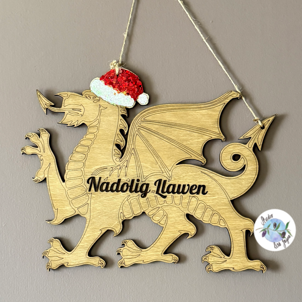 Wooden Christmas Welsh dragon ornament with a Santa hat and 'Nadolig Llawen' text Hanging on a brown wall