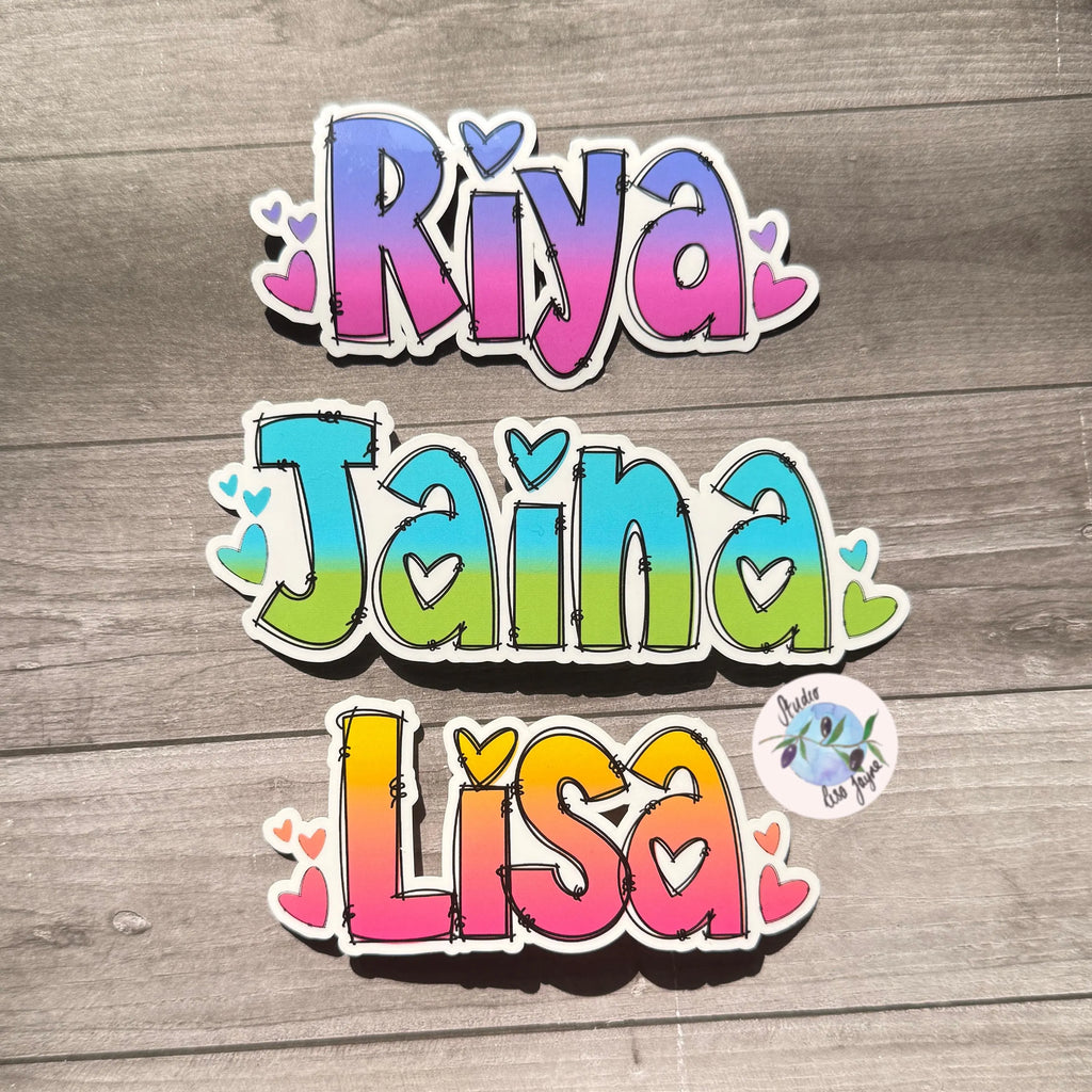 Ombré Colorful names stickers 'Riya', 'Jaina', 'Lisa' with heart designs on a wooden background