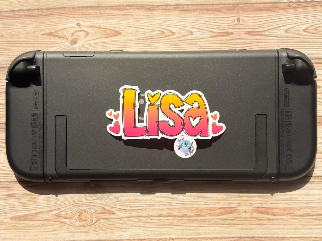Black gaming console with a colorful Ombré Heart 'Lisa' sticker on a wooden surface.  Nintendo Switch 2