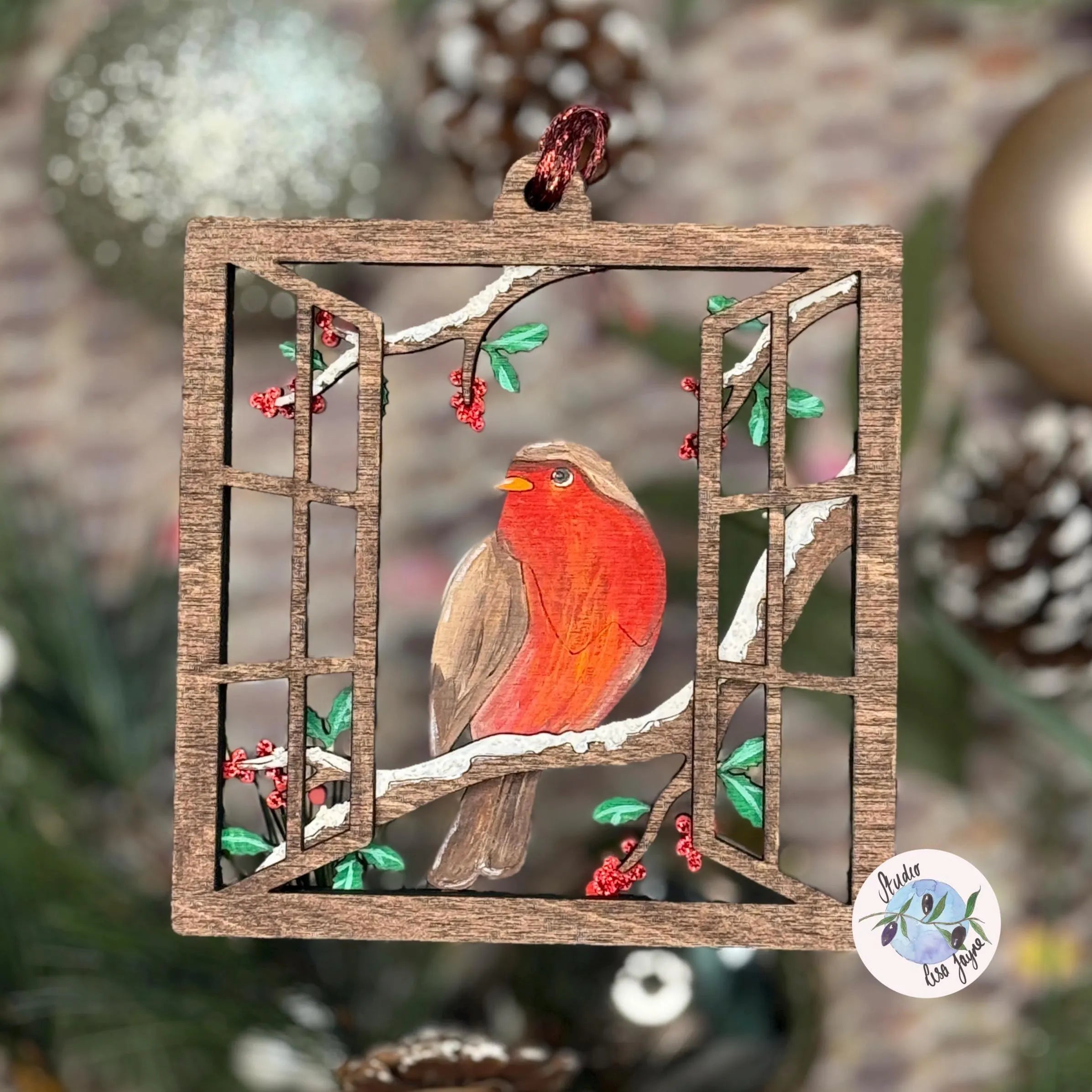 Decorative ornament with a robin on a branch, framed by wooden bars, against a blurred Christmas tree background.