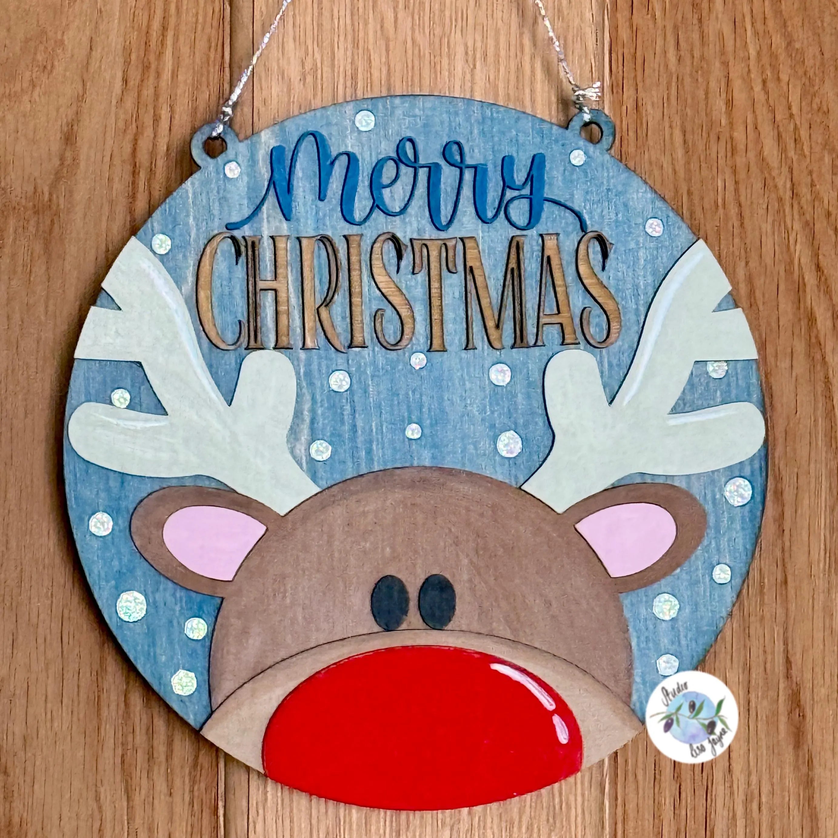 Decorative Christmas sign with reindeer face and 'Merry Christmas' text on a wooden background