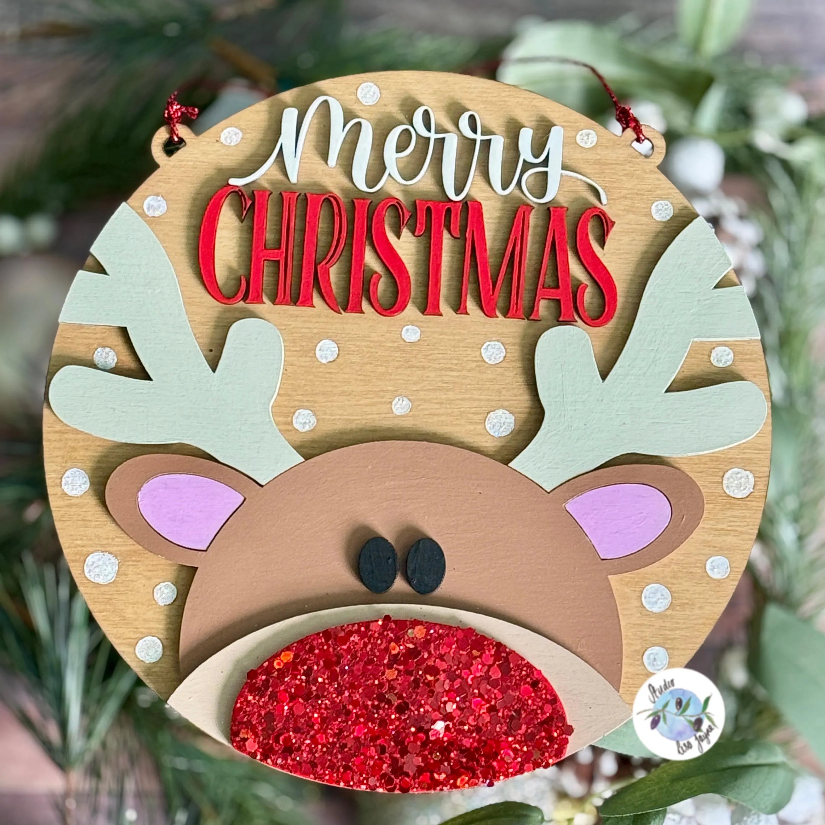 Wooden hand painted reindeer ornament with 'Merry Christmas' text on a green leafy background