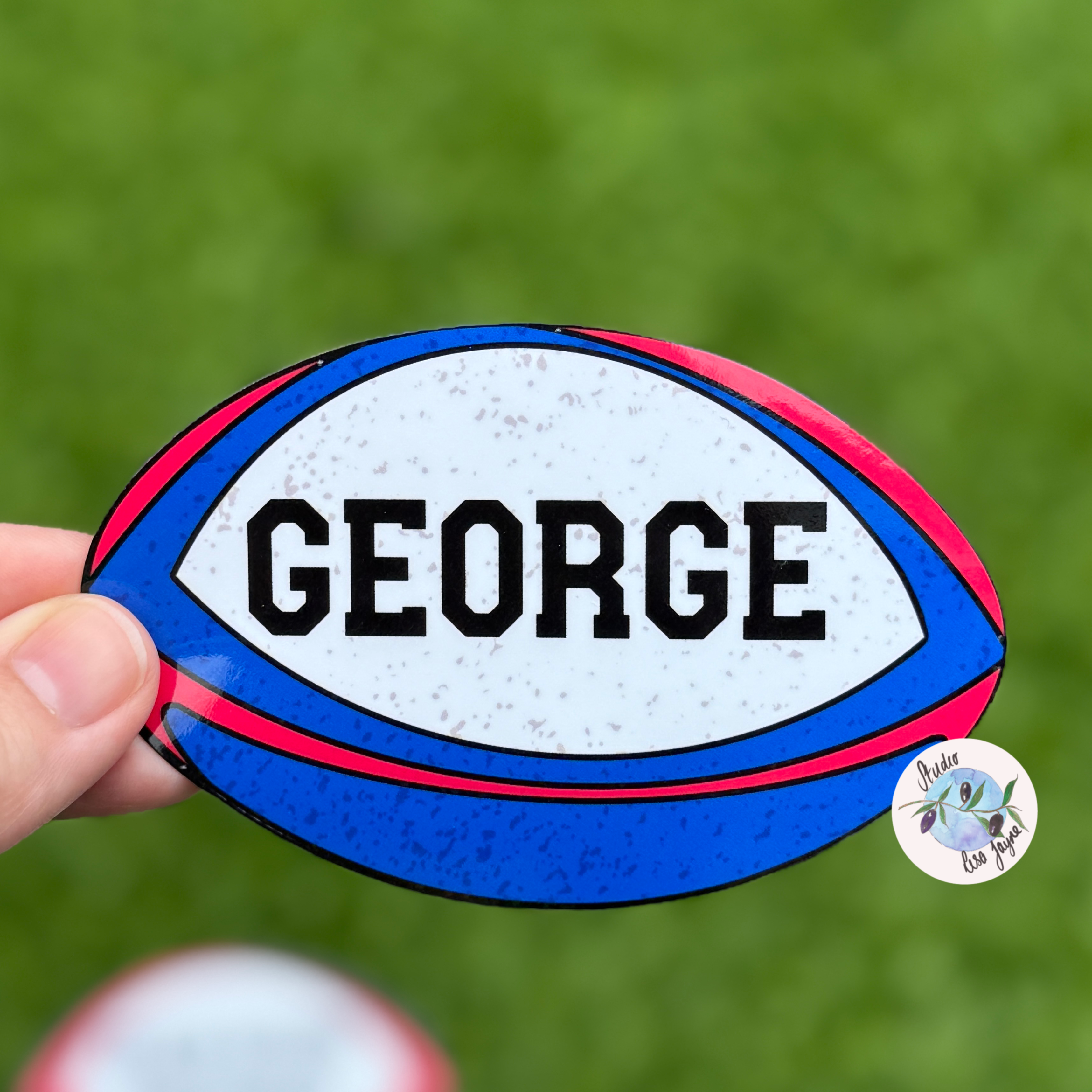 England rugby ball-shaped sticker with 'GEORGE' text held against a green background