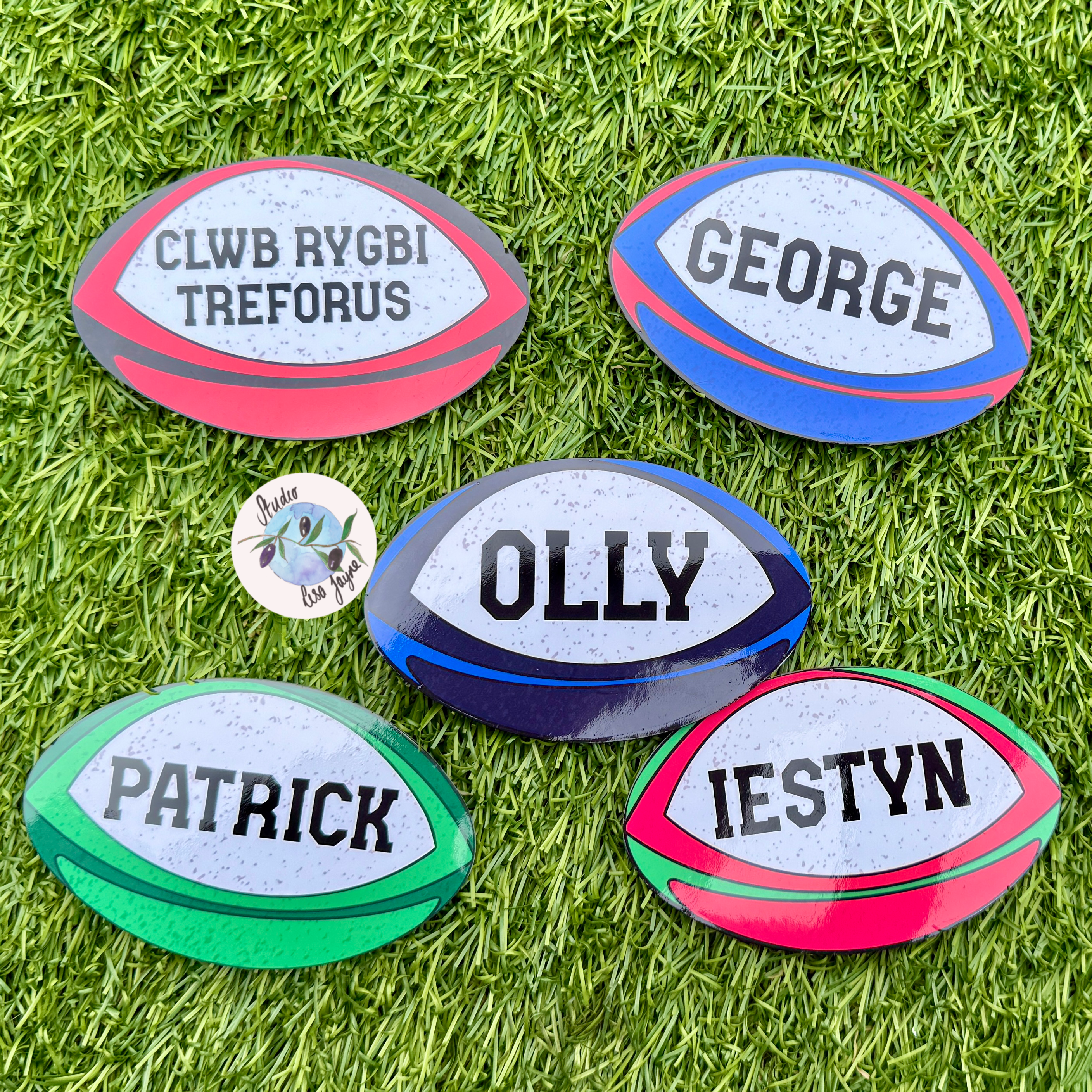 Five rugby ball-shaped stickers with personalised names , placed on grass.
