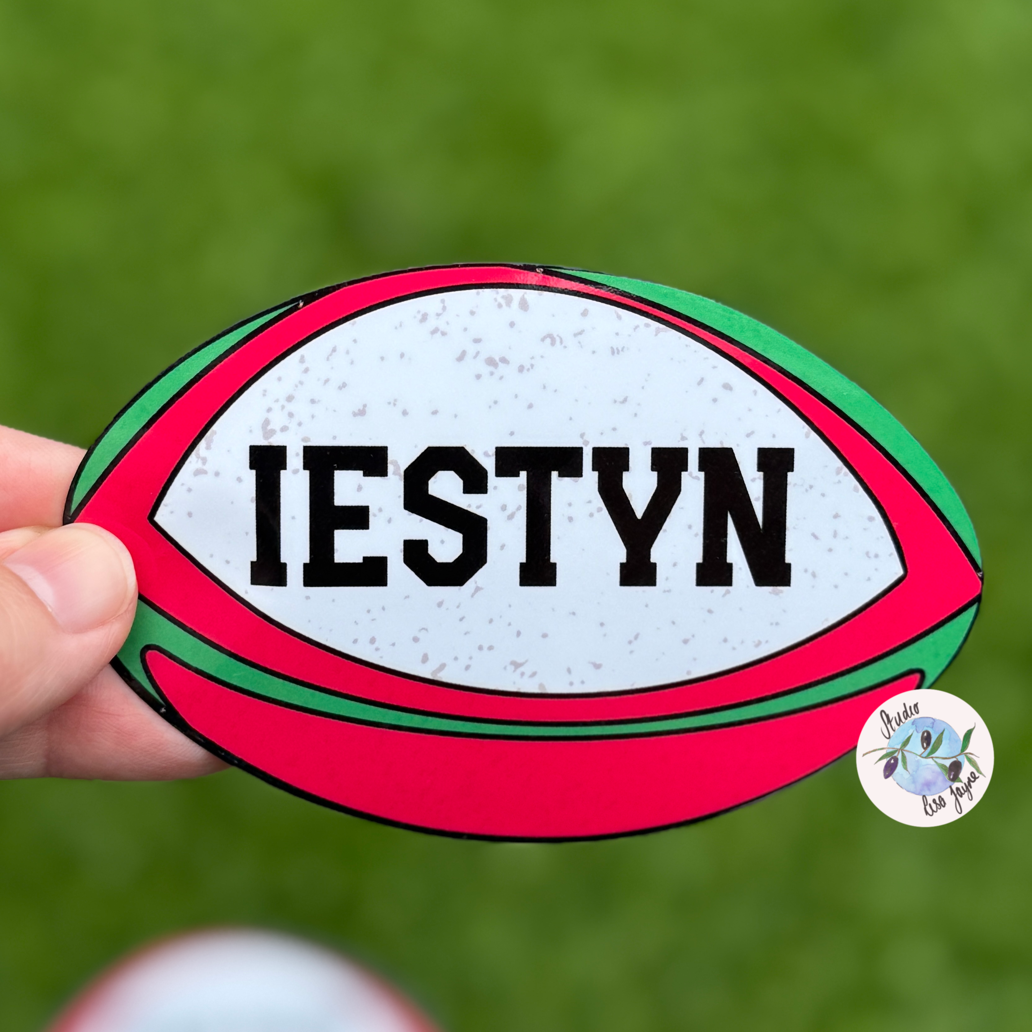 Welsh Rugby Ball Sticker with 'IESTYN' text held by a hand against a green background