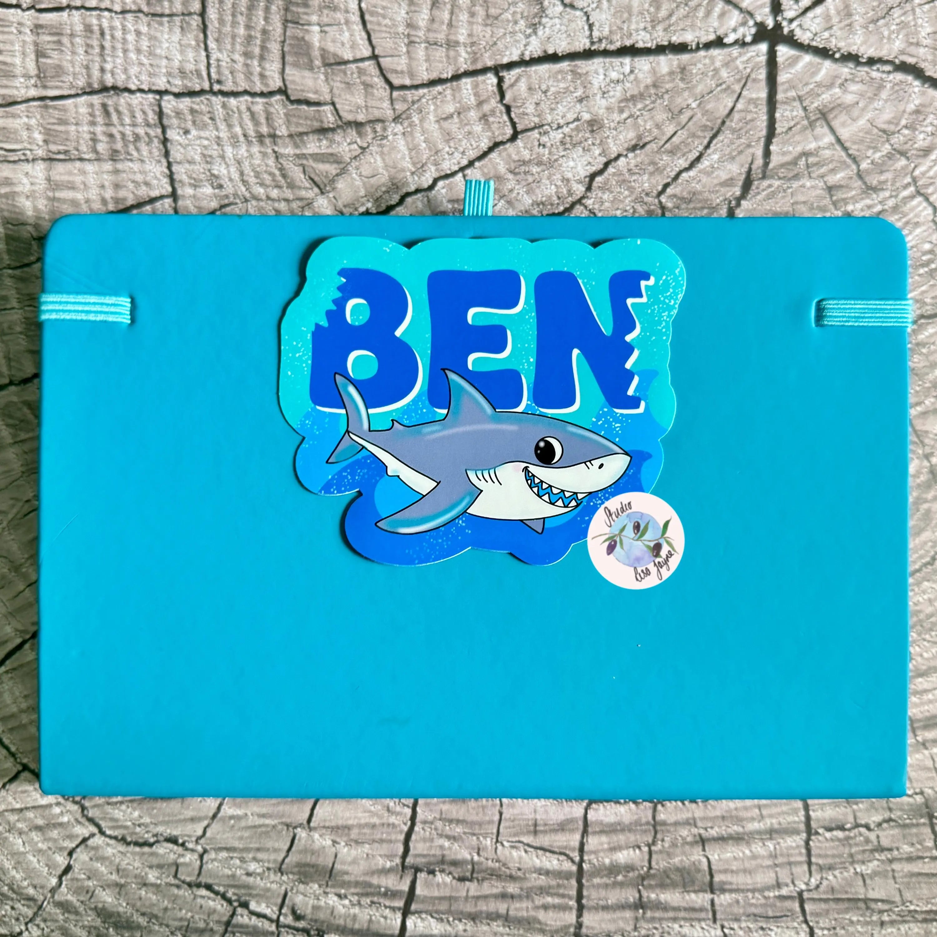 Blue notebook diary journa folder with 'BEN' and shark design on a wooden surface