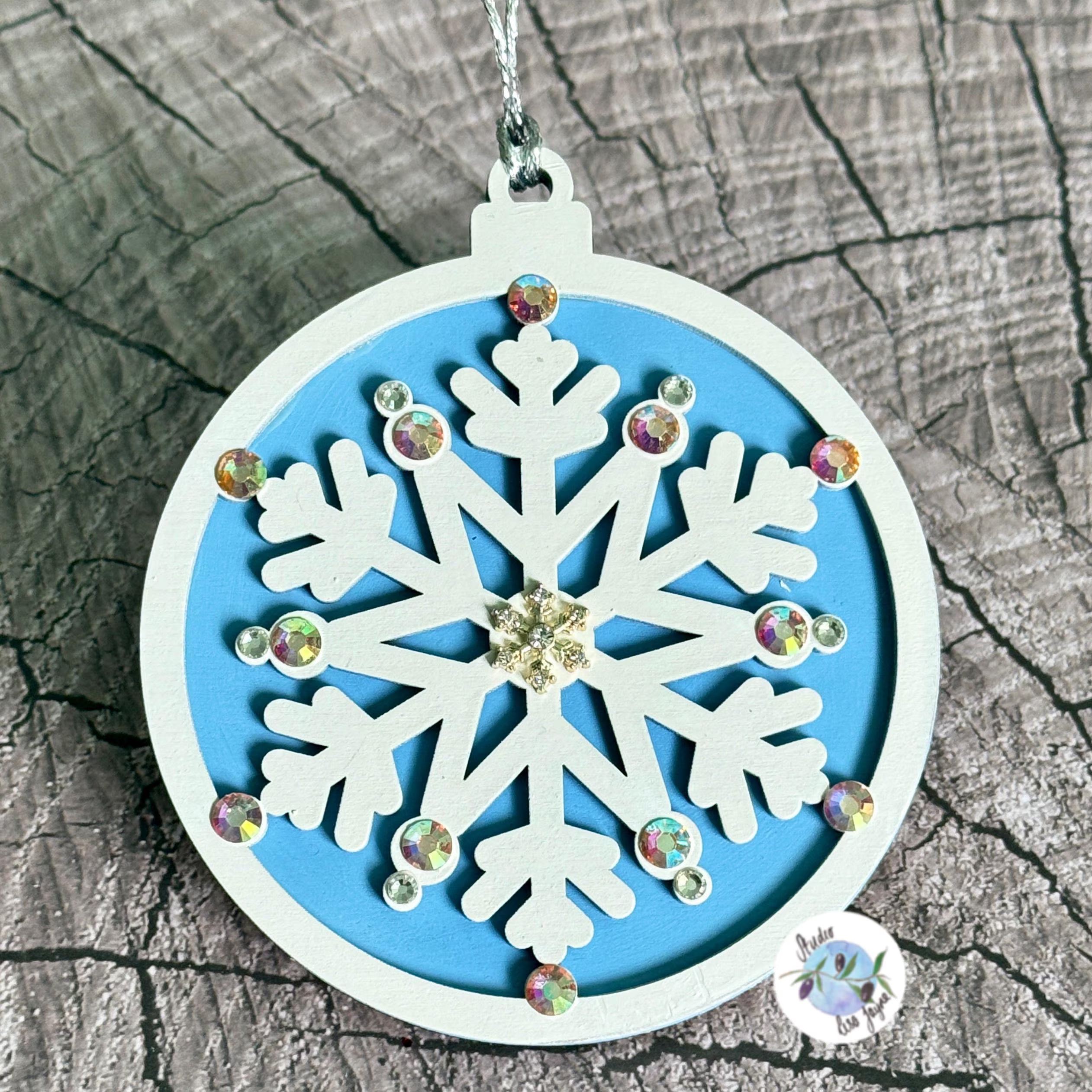 Decorative snowflake Christmas Tree decoration with rhinestones on a blue background, placed on a textured wooden surface.