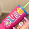 Pink tumbler with colourful unicorn sticker and a straw, held by a hand.