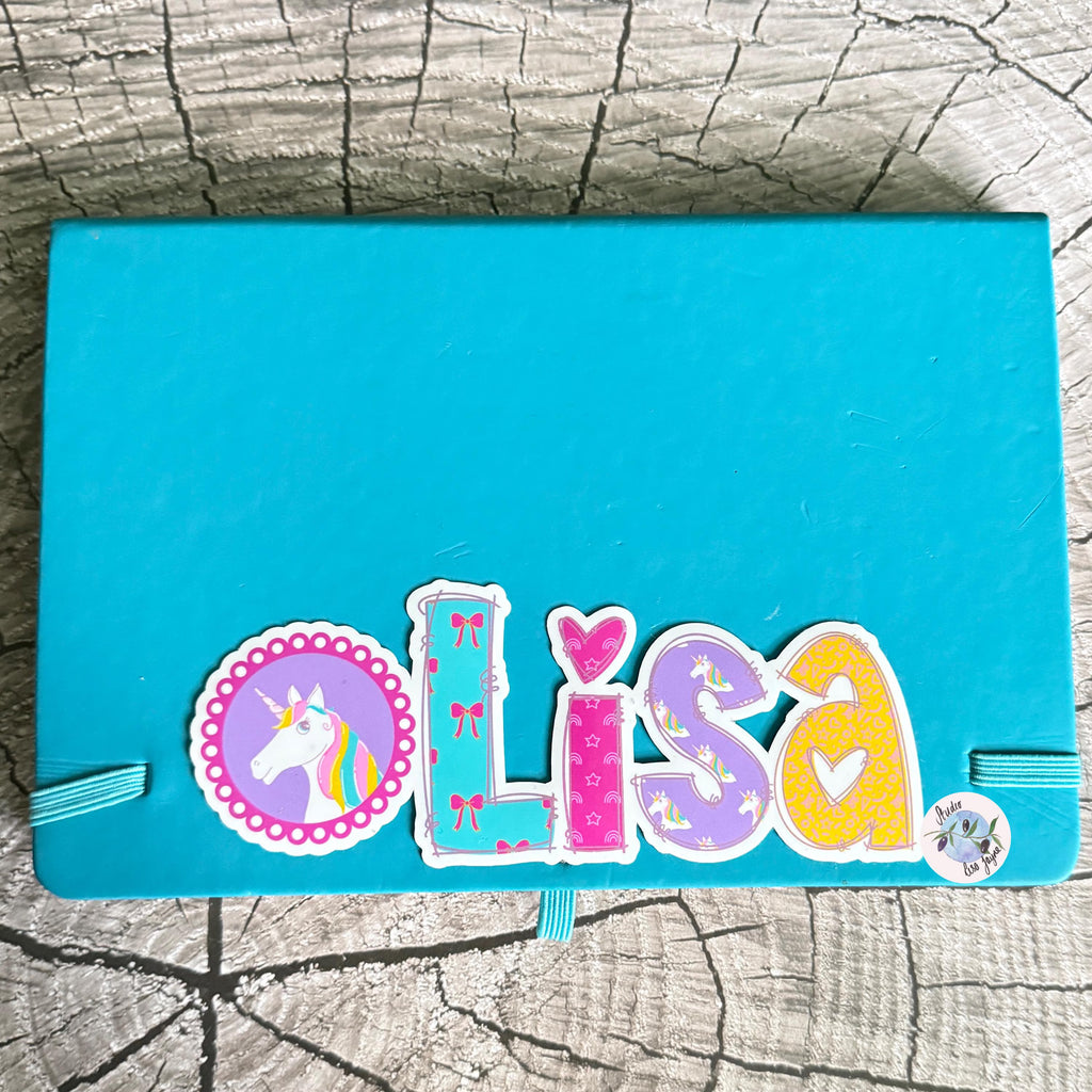 Blue notebook with decorative unicorn sticker spelling 'Lisa' on a textured surface