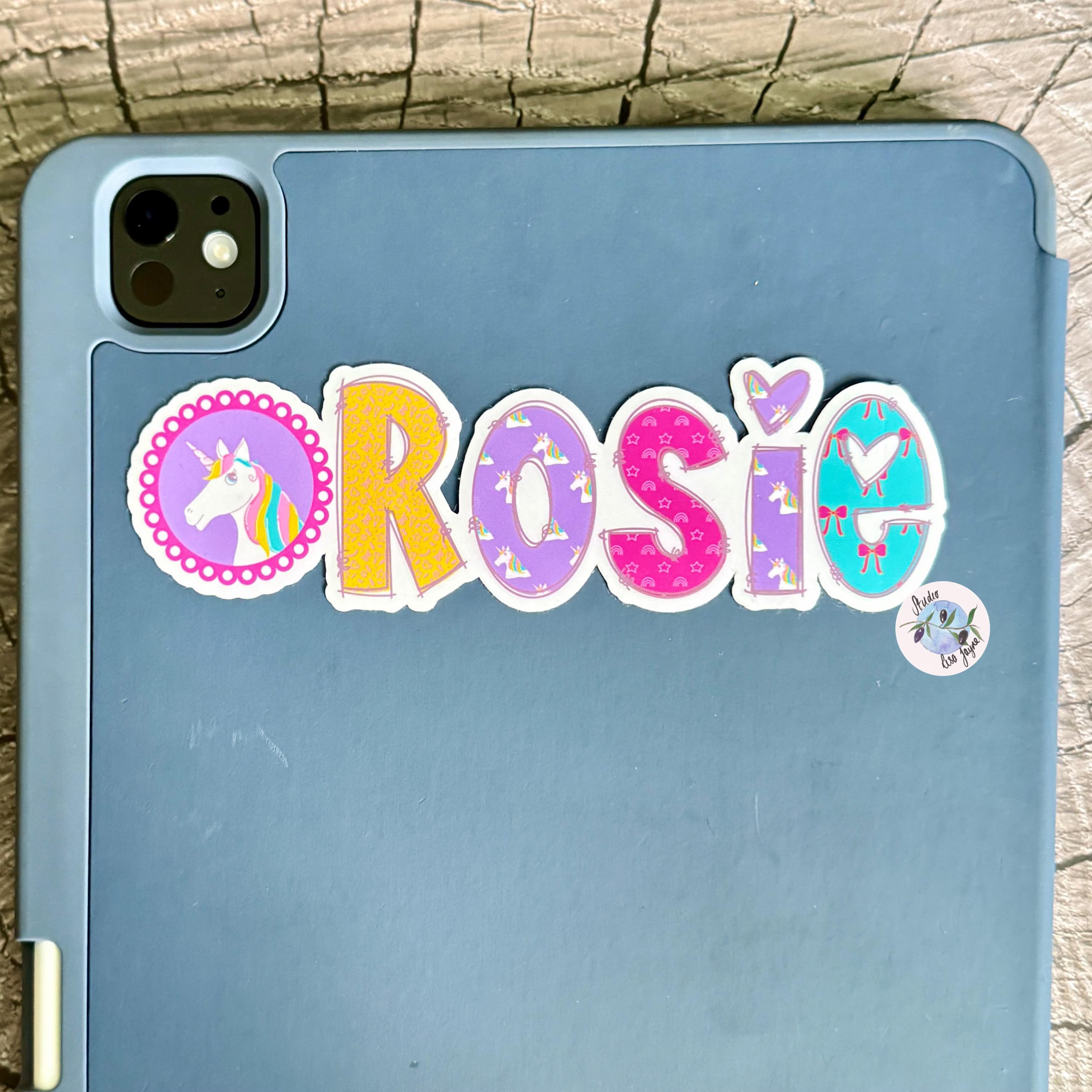 Blue ipad tablet with a colourful 'Rosie' unicorn sticker on a wooden surface