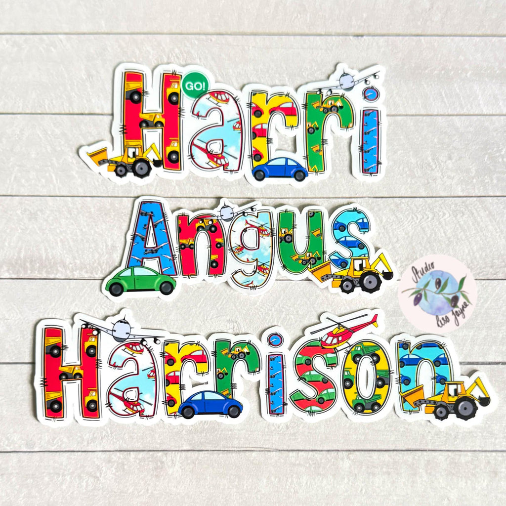 Colorful name stickers with vehicle designs on a light wooden surface.  Aeroplane, helicopter, cars, diggers