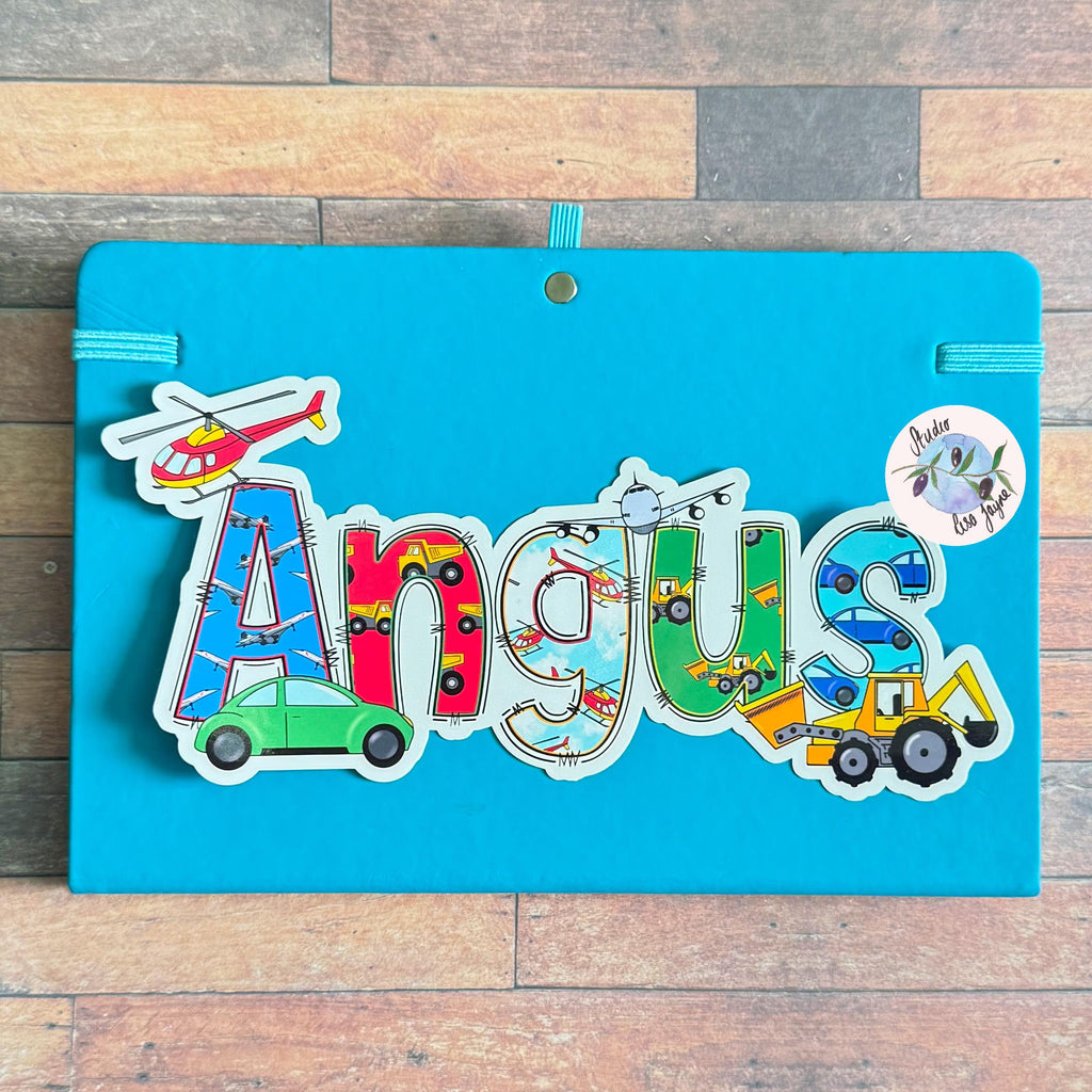 Colorful name plaque with 'Angus' and transportation-themed stickers on a wooden background