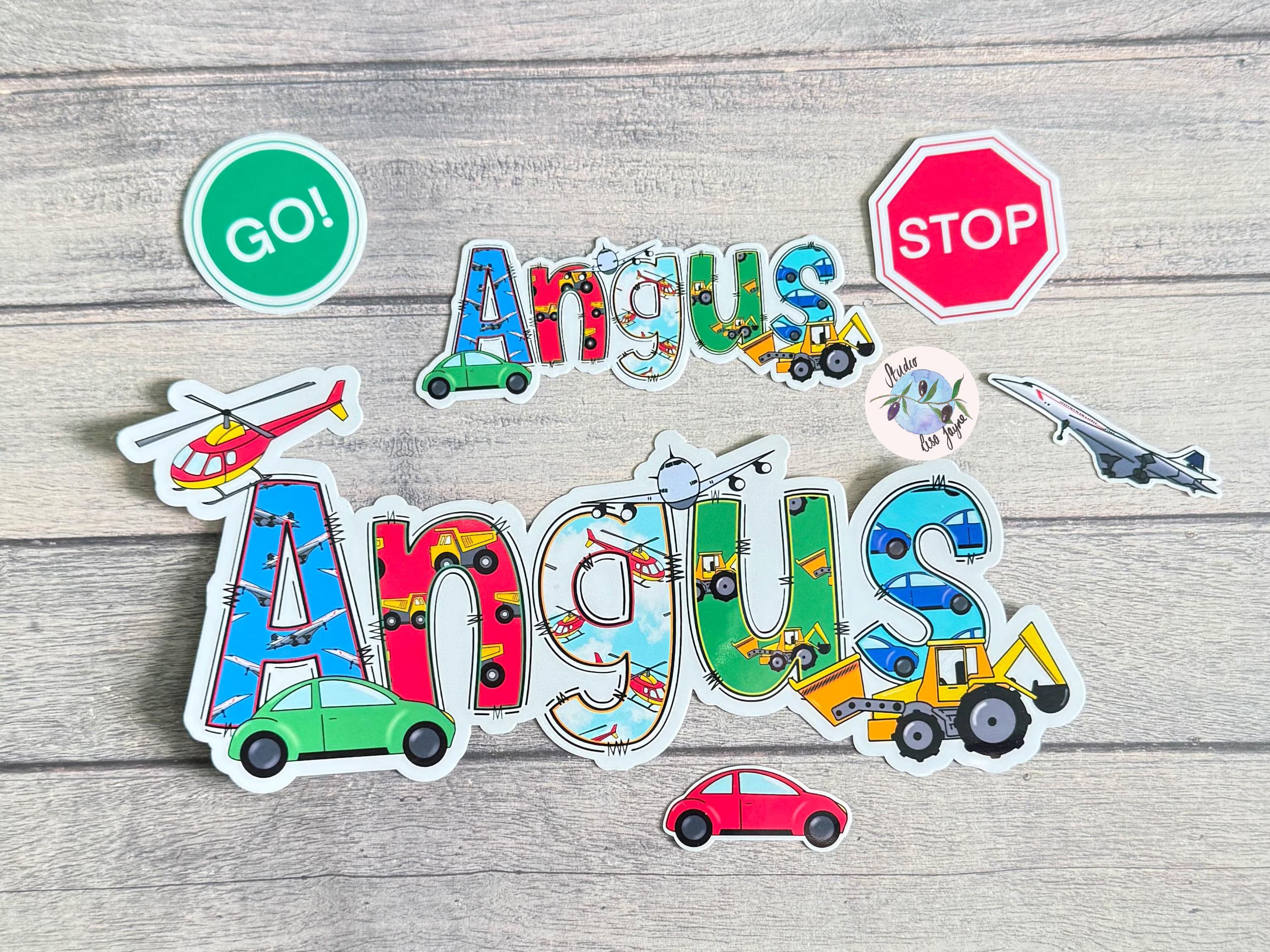 Colorful stickers with the name 'Angus' and various transportation-themed designs on a wooden surface.
