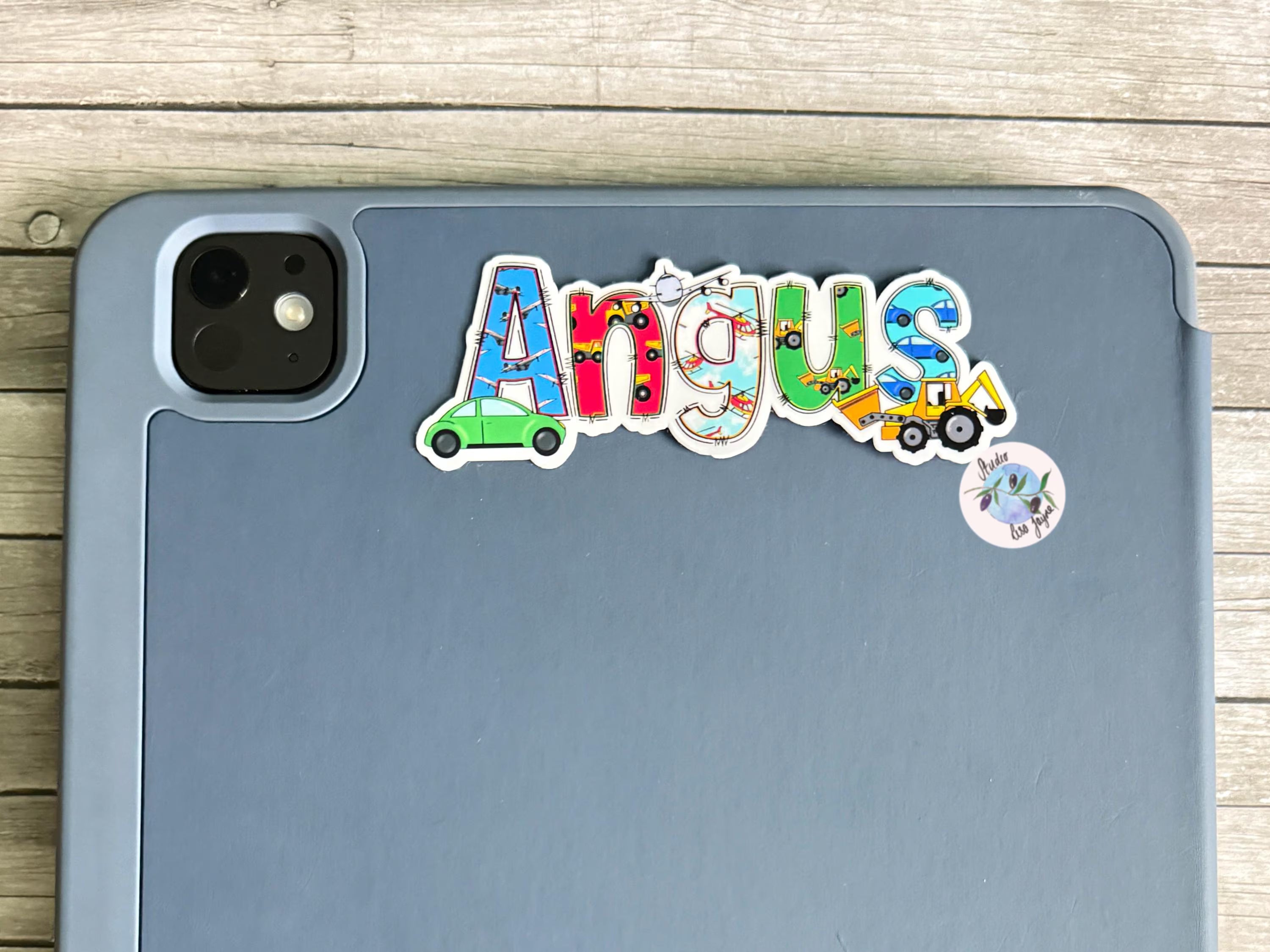Colorful 'Angus' vehicle stickers on a gray tablet with a wooden surface background