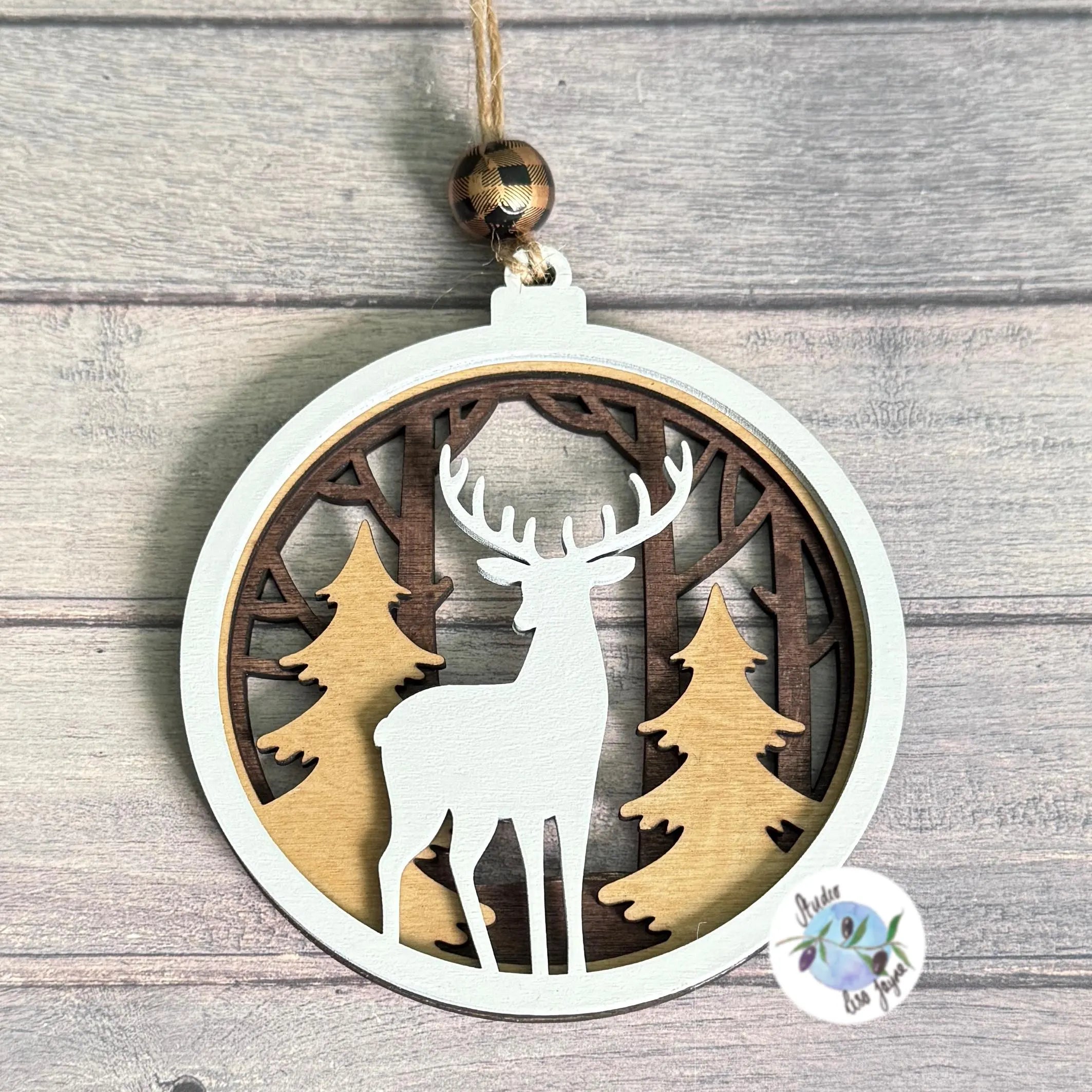 Xmas wooden ornament with a hand painted reindeer and forest design on a wooden surface.