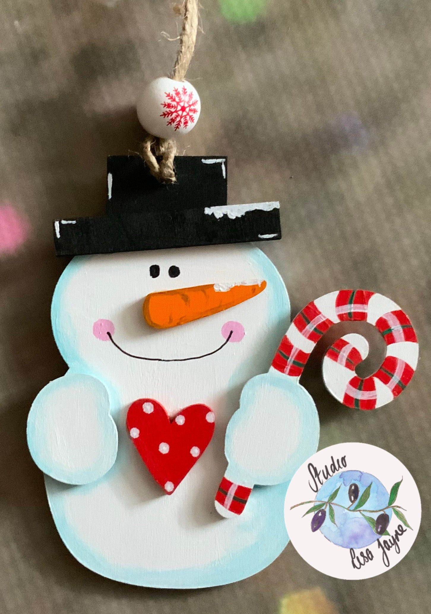 3D Hand Painted Snowman Christmas decoration holding a sugarcane with a polka dot red heart - Blurred Christmas lights