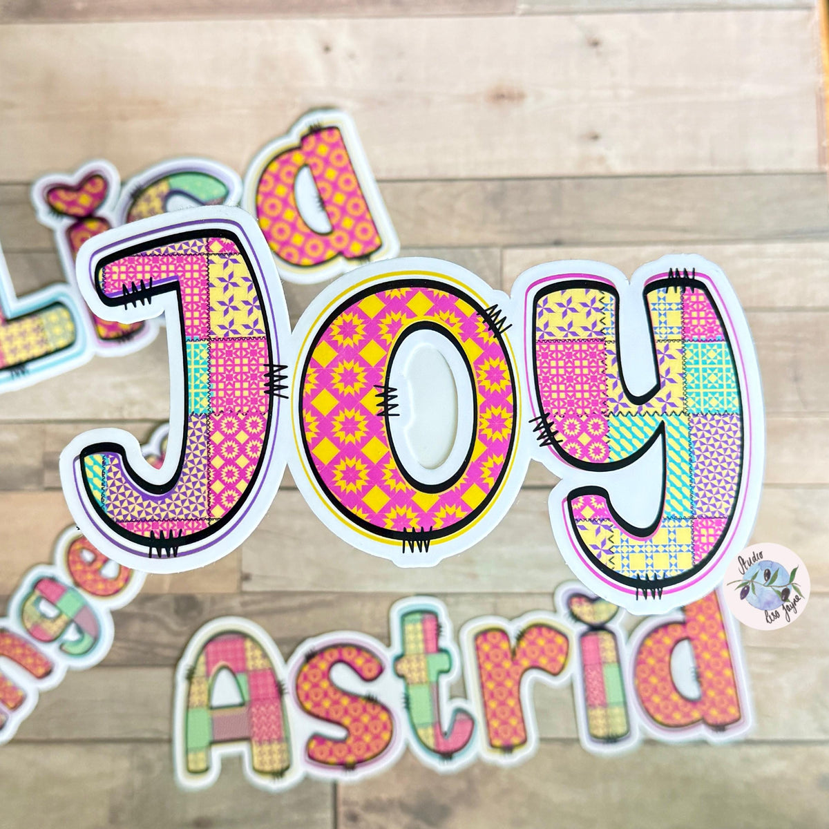 Patchwork Style Name Sticker Label - a group of colorful letters on a wood surface